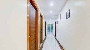 A corridor with wooden doors, white walls, and a marble-tiled floor. - The Grand Homes (Lucknow)