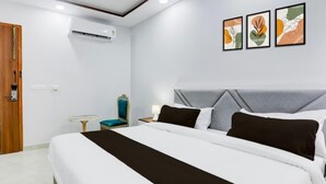 A hotel room with a large bed, a bedside table, a chair, and a wall-mounted air conditioner. - The Grand Homes (Lucknow)