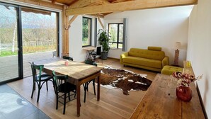 A spacious room with a wooden ceiling, a dining table with chairs, a yellow sofa, a cowhide rug, and a vase with flowers.