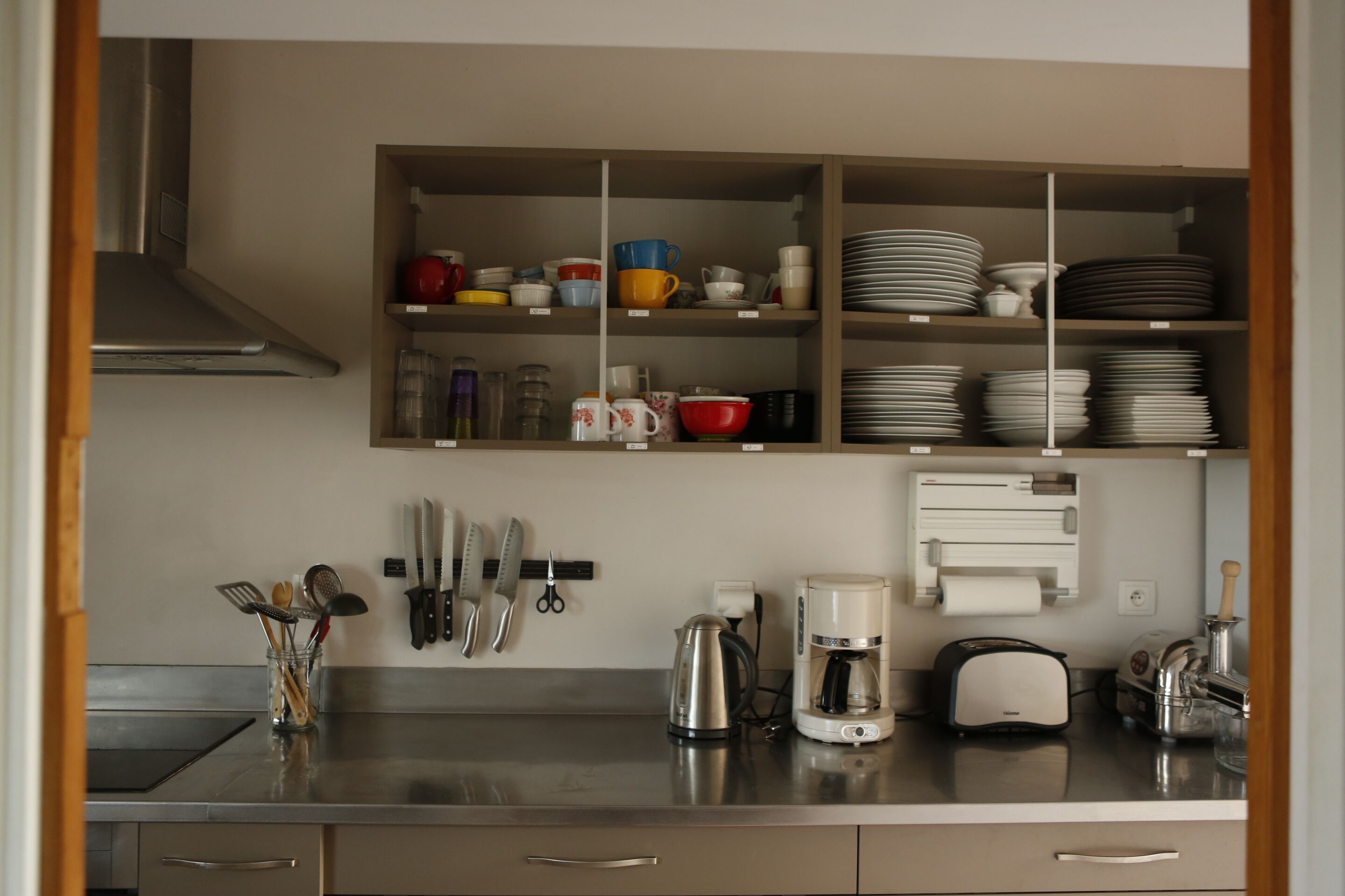 Una cocina moderna con electrodomésticos de acero inoxidable, cafetera y estantes ordenados con vajilla y utensilios.