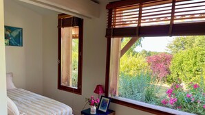 Un dormitorio con cama, una ventana con contraventanas de madera, una mesita de noche con lámpara y un cuadro en la pared.