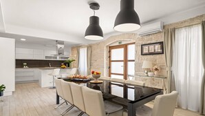 A modern kitchen with white cabinets, a central island, and a dining area with a glass table and chairs. - Villa Gambin (100121-K1) - Kastelir (Kastelir)