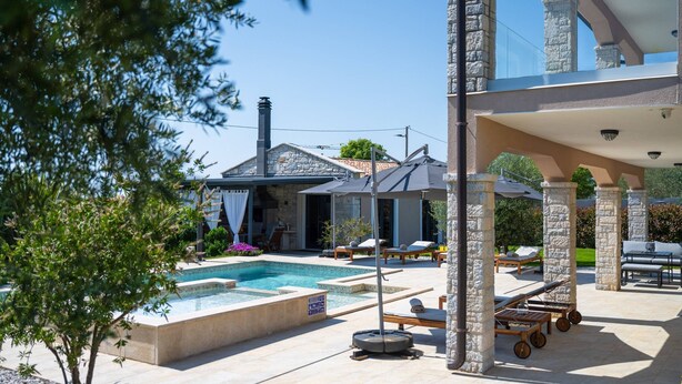 A pool area with lounge chairs and umbrellas, stone pillars, and a stone building in the background. - Villa Gambin (100121-K1) - Kastelir (Kastelir)
