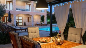 An outdoor dining area with a pool view, stone pillars, and a wooden table with chairs. - Villa Gambin (100121-K1) - Kastelir (Kastelir)