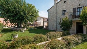 A stone building with a balcony, surrounded by a well-maintained garden with a lawn and flowering plants. - Villa Radetići (100431-K1) - Tinjan (Tinjan)