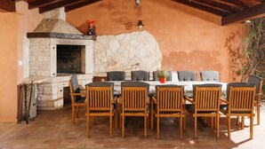 An outdoor patio with a stone fireplace, wooden chairs, and a table. - Villa Radetići (100431-K1) - Tinjan (Tinjan)