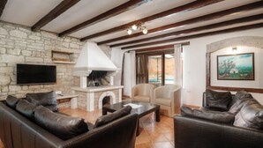 A living room with a stone wall, fireplace, leather sofas, and a flat-screen TV. - Villa Radetići (100431-K1) - Tinjan (Tinjan)