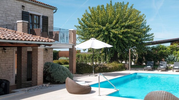 A pool area with a clear blue pool, lounge chairs, and a large tree. - Villa Radetići (100431-K1) - Tinjan (Tinjan)