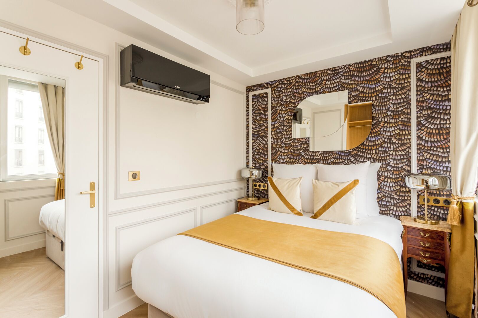 Une chambre d’hôtel avec un lit, un grand miroir, une télévision et un mur décoré d’un motif.