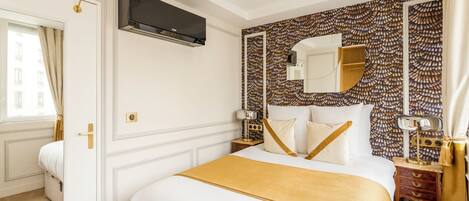 A hotel room with a bed, a large mirror, a TV, and a patterned wall.