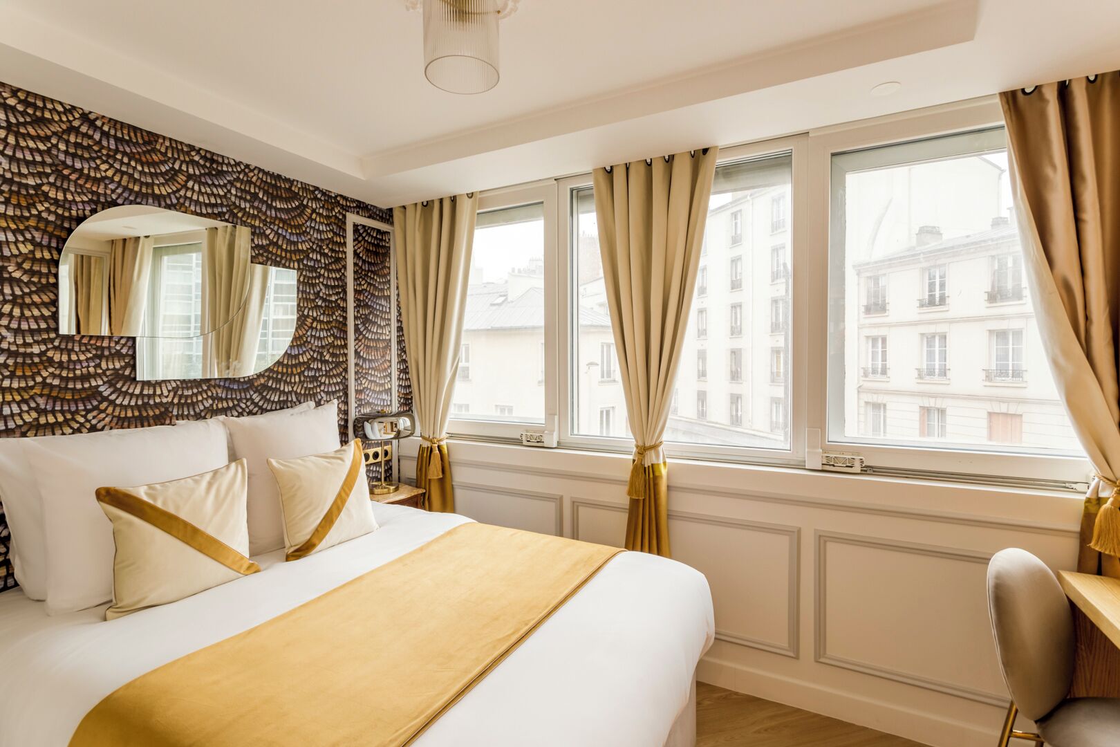 Una camera d'albergo con un letto grande, una scrivania, una sedia, uno specchio e vista sui palazzi dalla finestra.