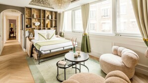Ein modernes Schlafzimmer mit Bett, Nachttisch und rundem Tisch. Ein Fenster mit Vorhängen, eine Chandelier und Blick auf Gebäude im Freien.
