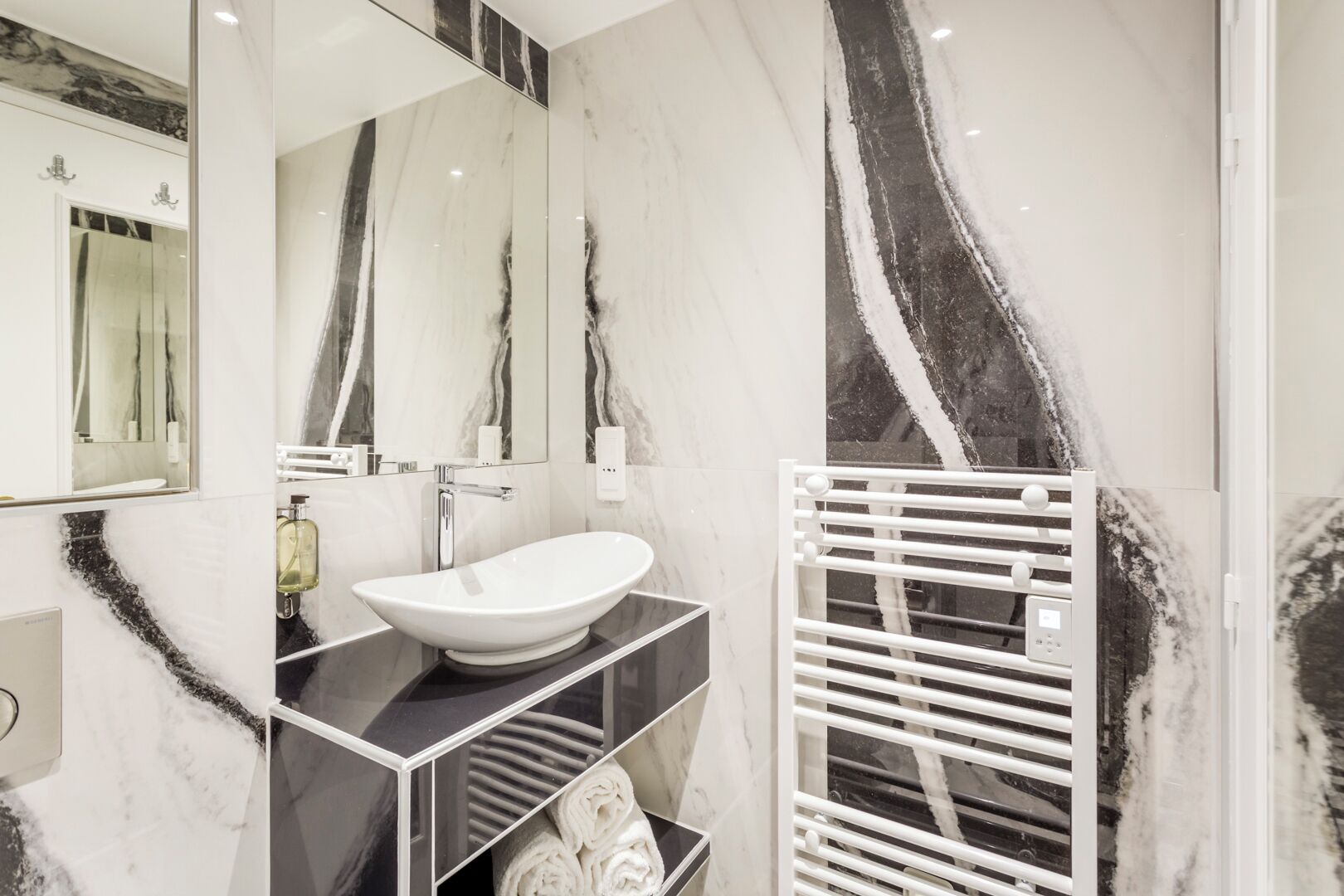 A modern bathroom with a white sink, marble walls, and a towel rack.