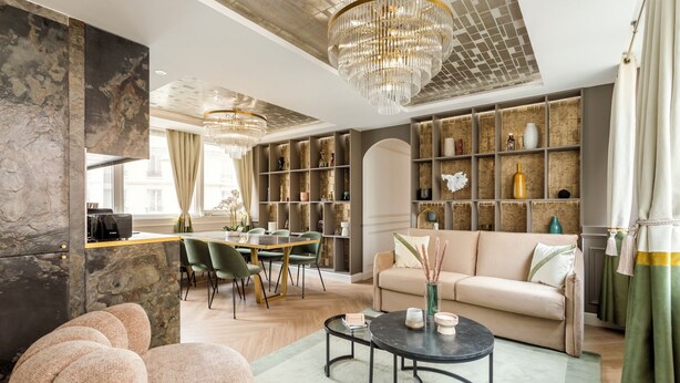 Ein modernes Wohnzimmer mit Sofa, Couchtisch und Sesseln. Es gibt einen Essbereich mit Tisch und Stühlen. Der Raum verfügt über eine Chandelier und Regale mit Dekorationen.