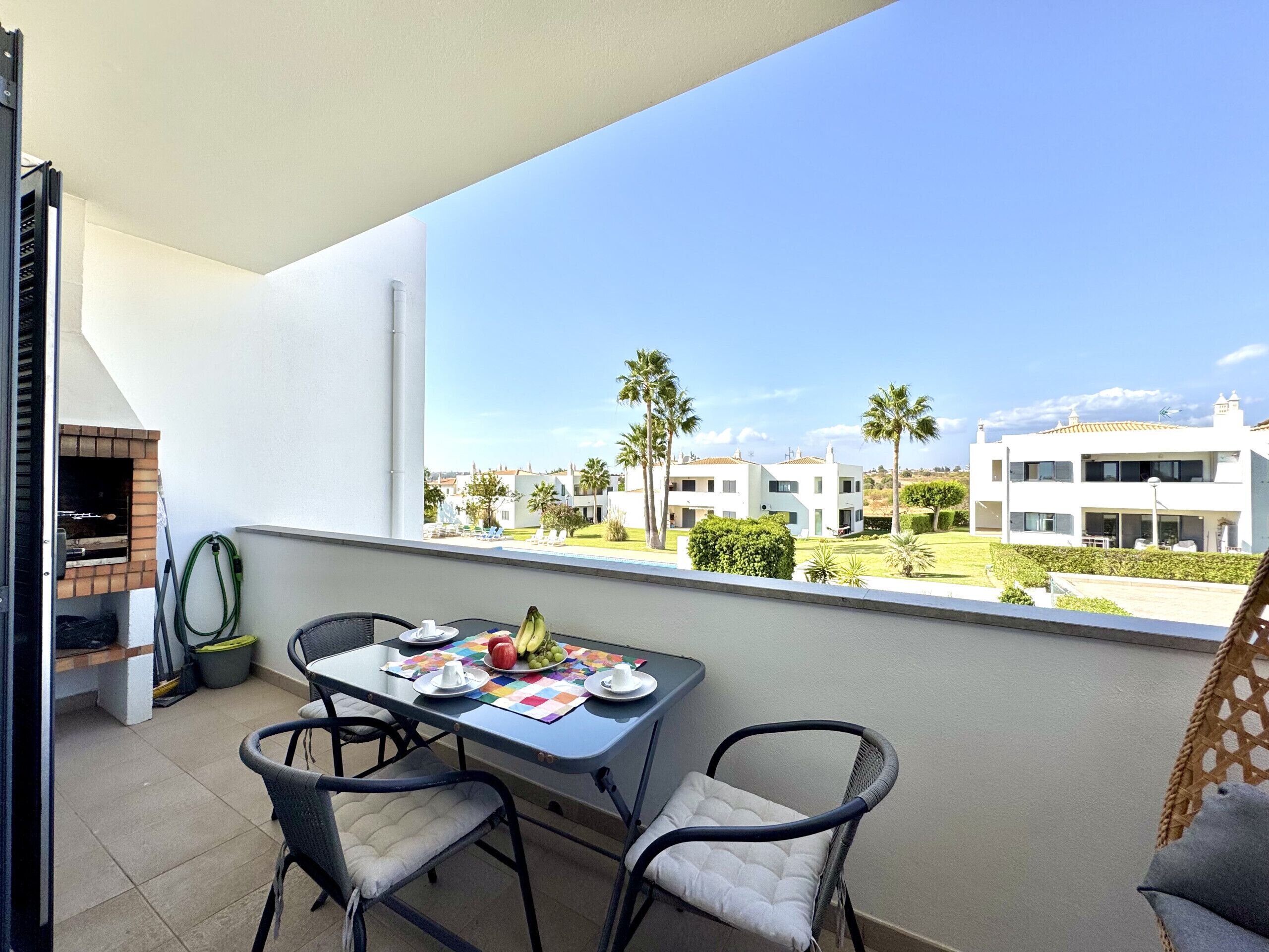 A balcony with a table set for two, a grill, and a view of modern buildings.