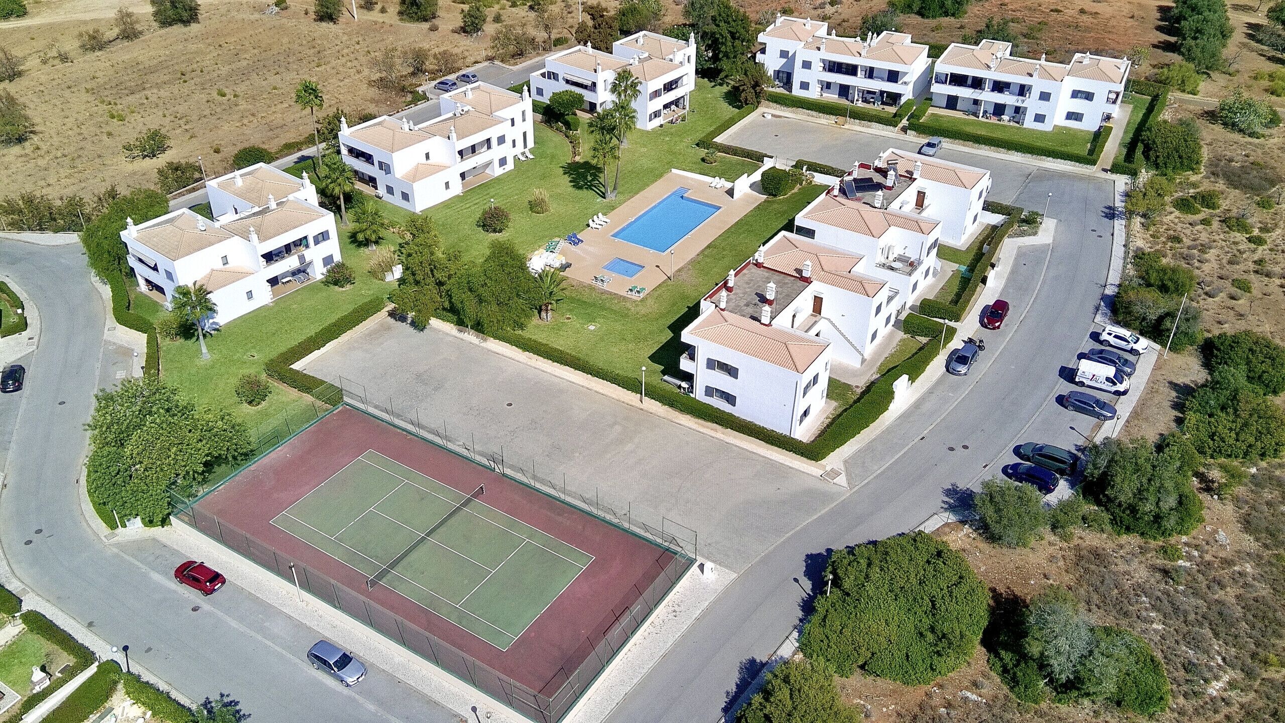 A residential area with modern white buildings, a tennis court, and a swimming pool.