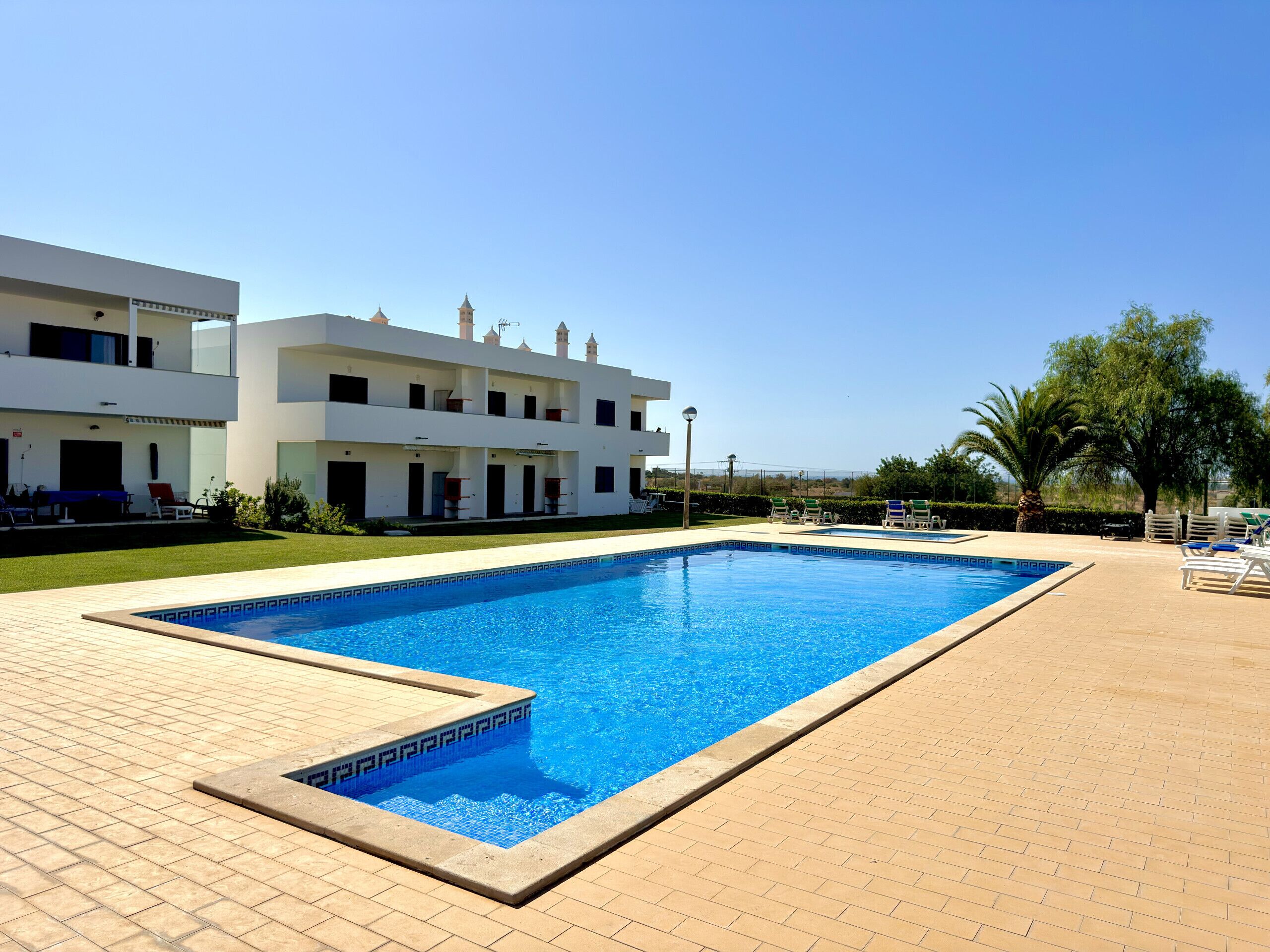 Una piscina rectangular con borde de azulejos, rodeada por un patio de ladrillo.