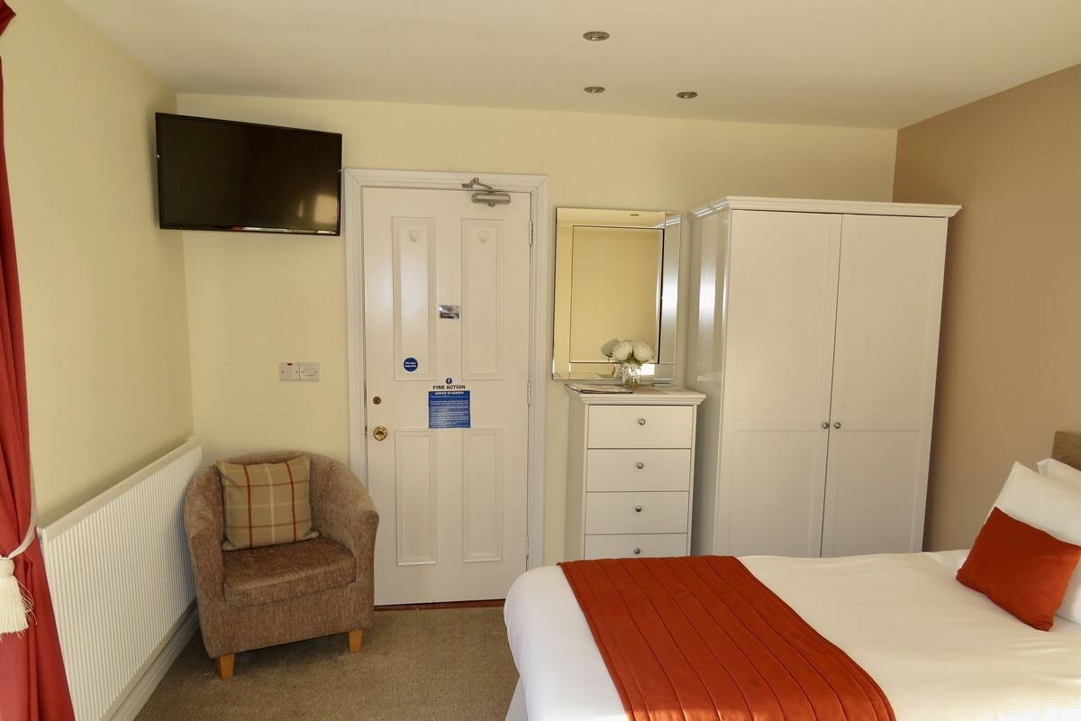A hotel room with a bed, a chair, a wardrobe, a dresser, a mirror, and a television.