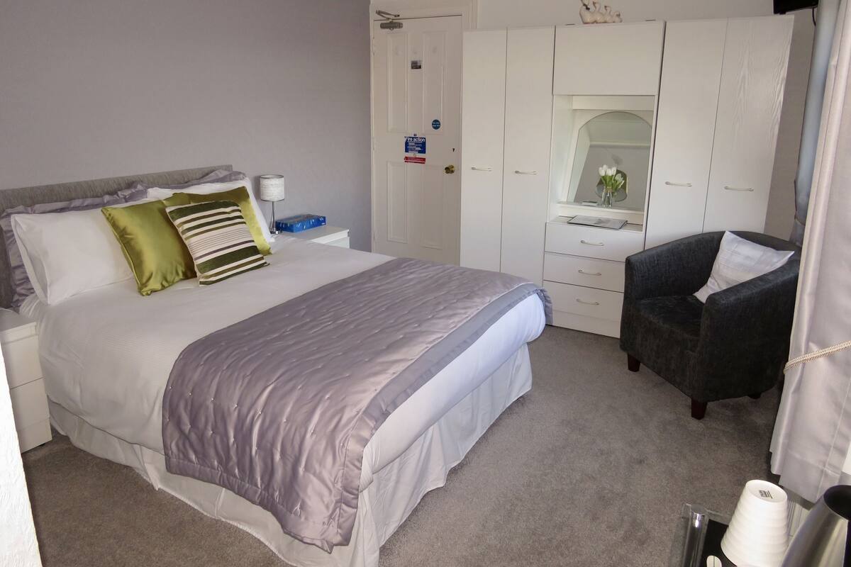 A bedroom with a bed, a chair, a wardrobe, and a mirror.