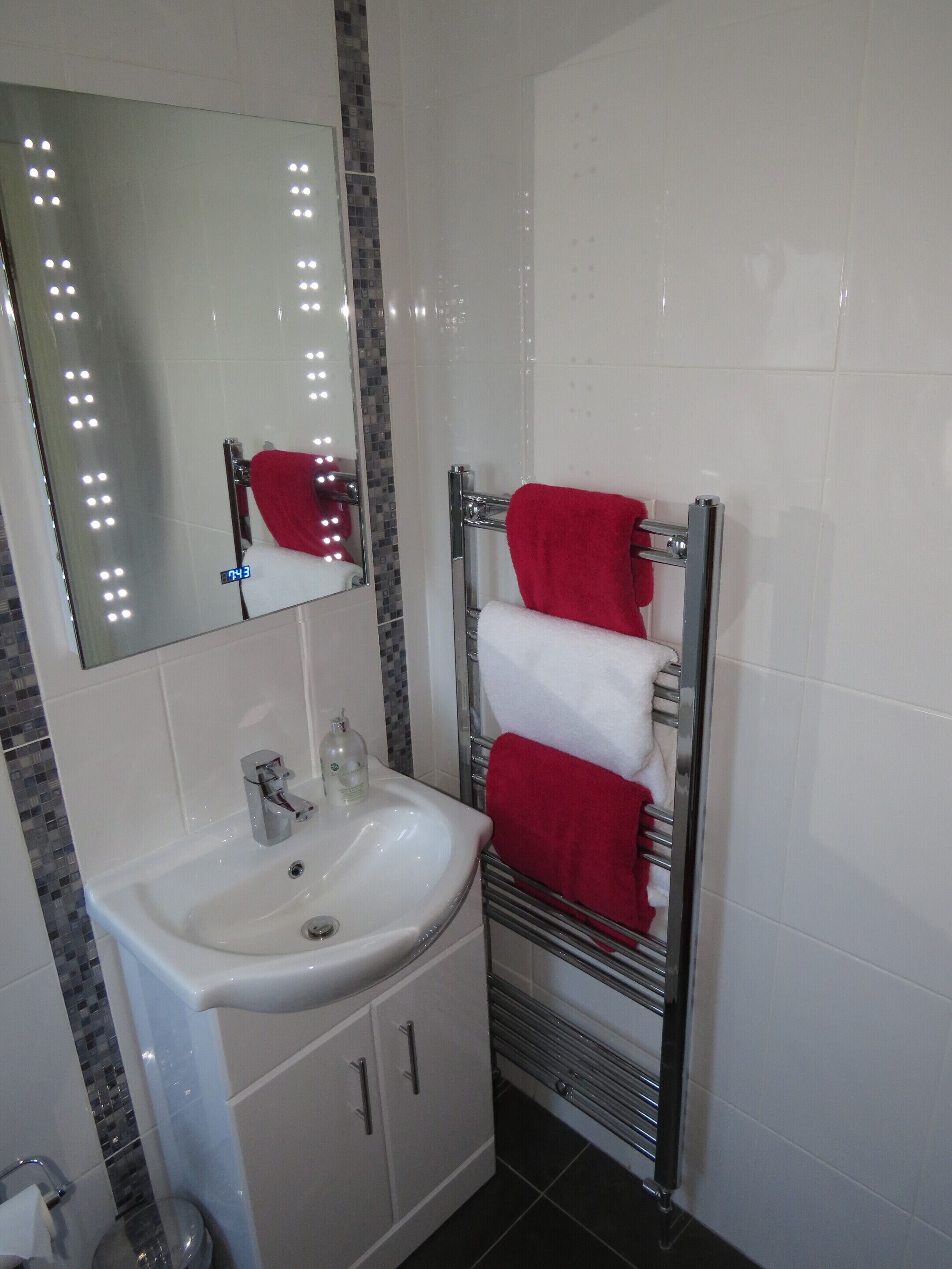 A bathroom with a white sink, a mirror, and a towel rack with red and white towels.
