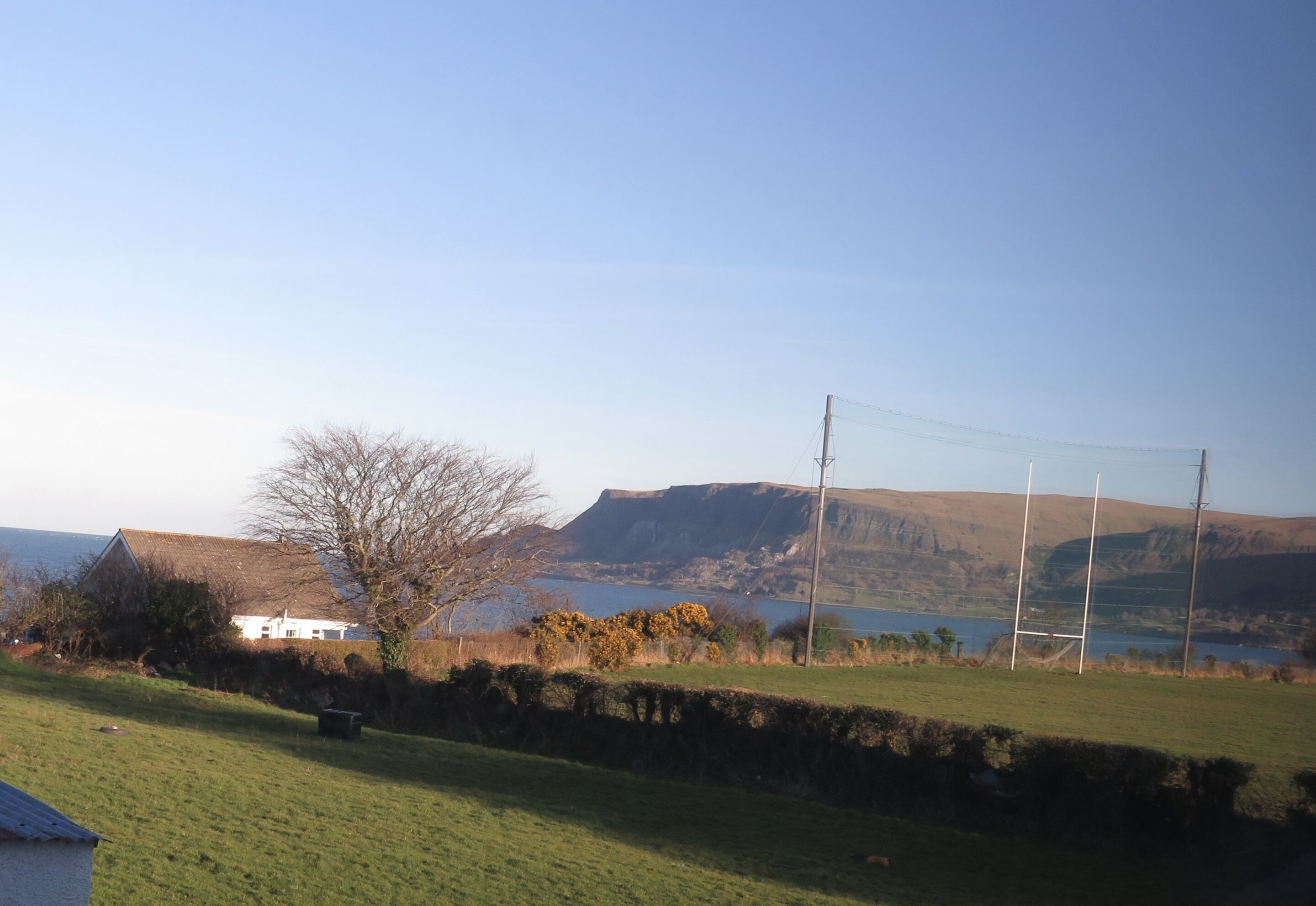 A rural landscape with a house, a stone wall, and a rugby field.