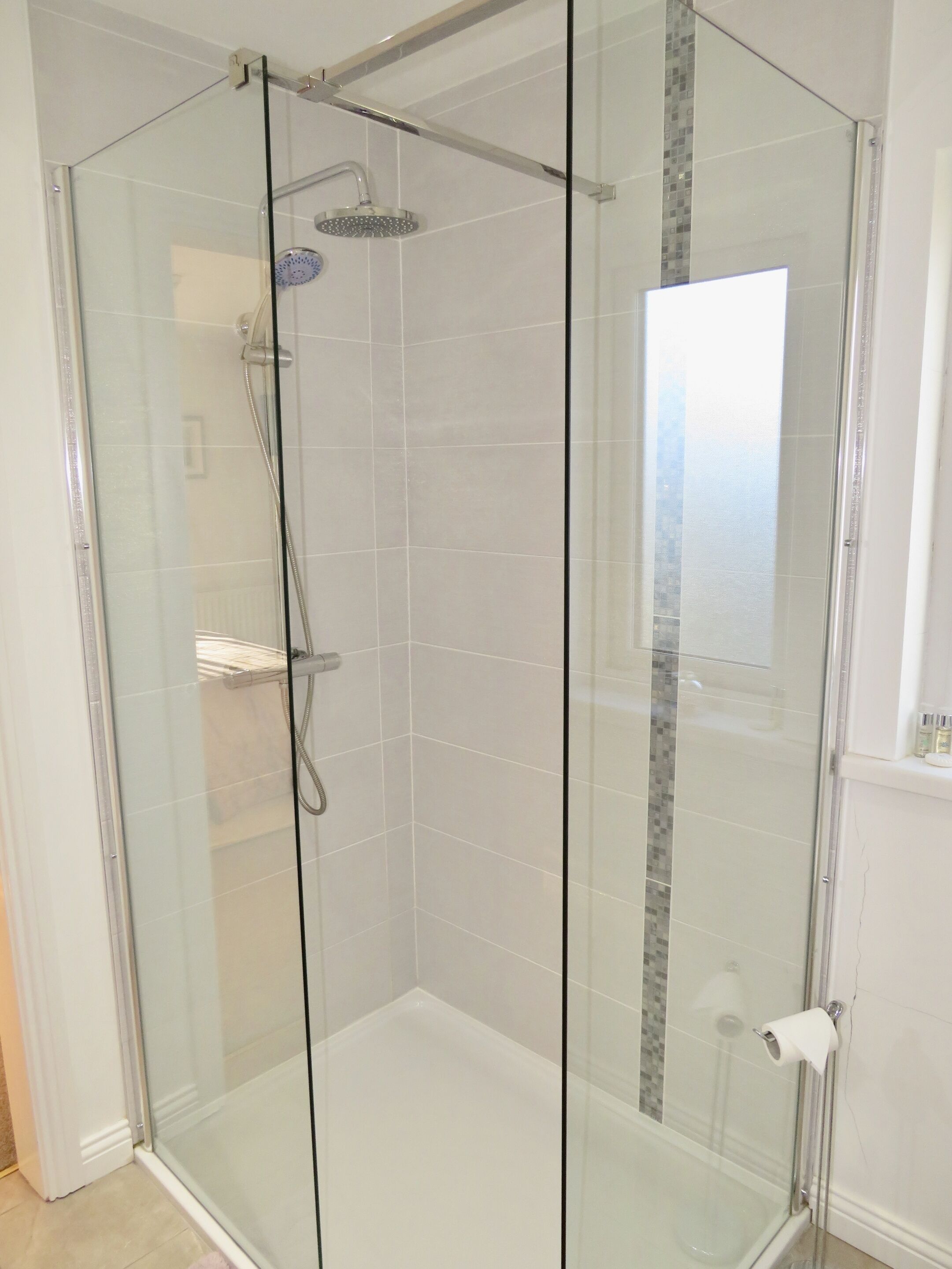 A glass-enclosed shower with a handheld showerhead and a wall-mounted faucet.