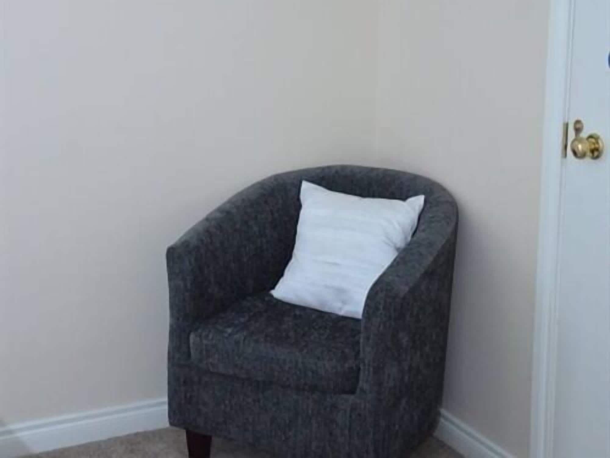 Un fauteuil d’angle avec un coussin blanc, placé contre un mur uni.