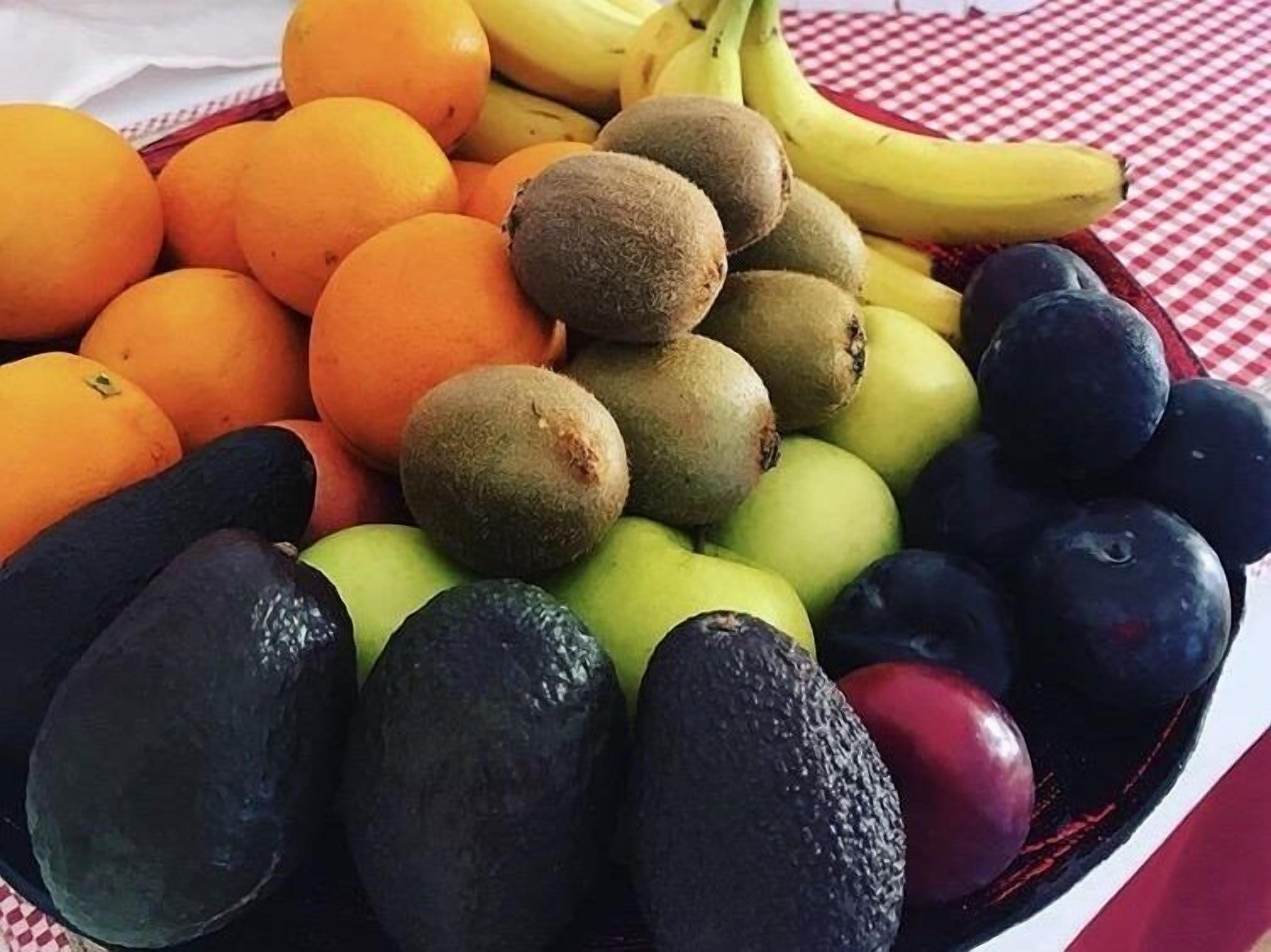 Una varietat de fruites, com ara taronges, plàtans, kiwis, pomes i présims, disposades sobre una taula.
