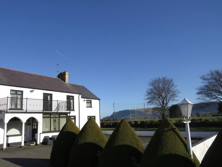 A white building with a balcony, surrounded by neatly trimmed conical hedges.