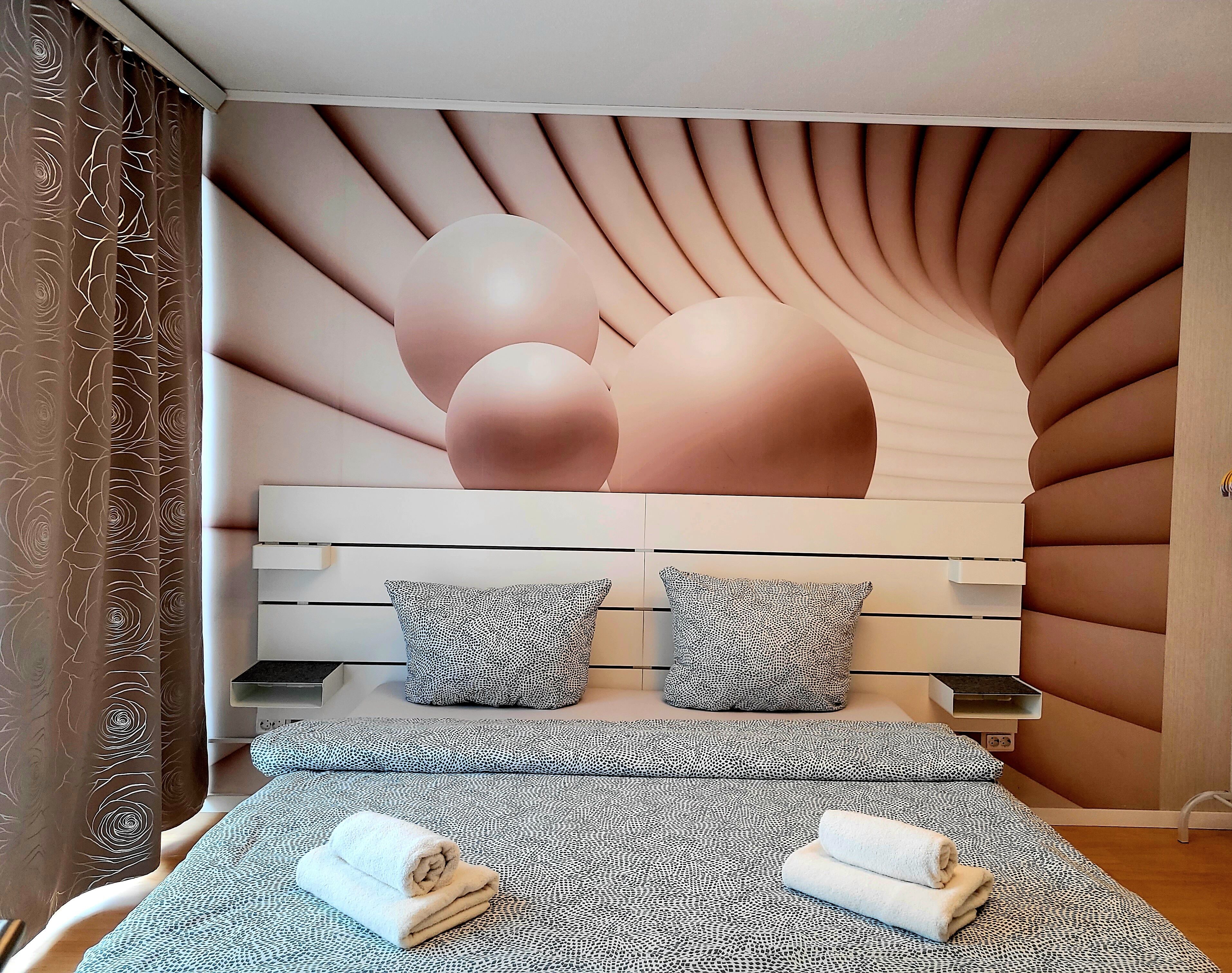 Ein modernes Schlafzimmer mit einem gewölbten Kopfteil, einem Bett mit gemusterten Betttextilien und zwei Kissen.