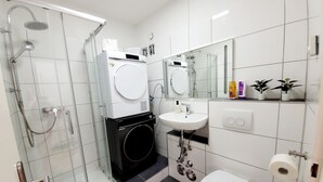 Une salle de bain moderne dotée d’une douche à parois de verre, d’un lave-linge encastré, d’un lavabo et de toilettes.