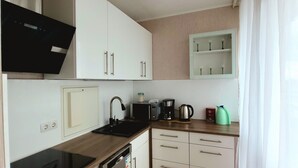 Une cuisine moderne avec des meubles blancs, une cuisinière noire, un lave-vaisselle et une machine à café.