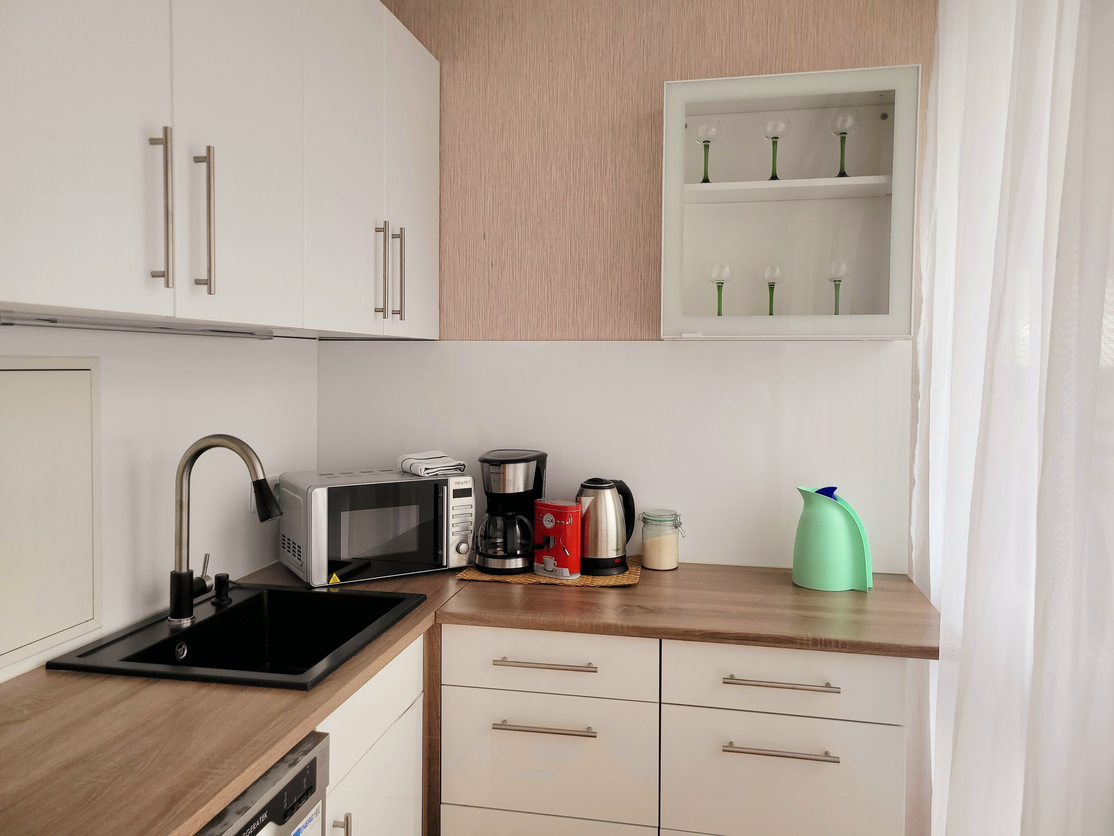Een moderne keuken met een magnetron, koffiezetapparaat en een groene kan op het aanrecht.
