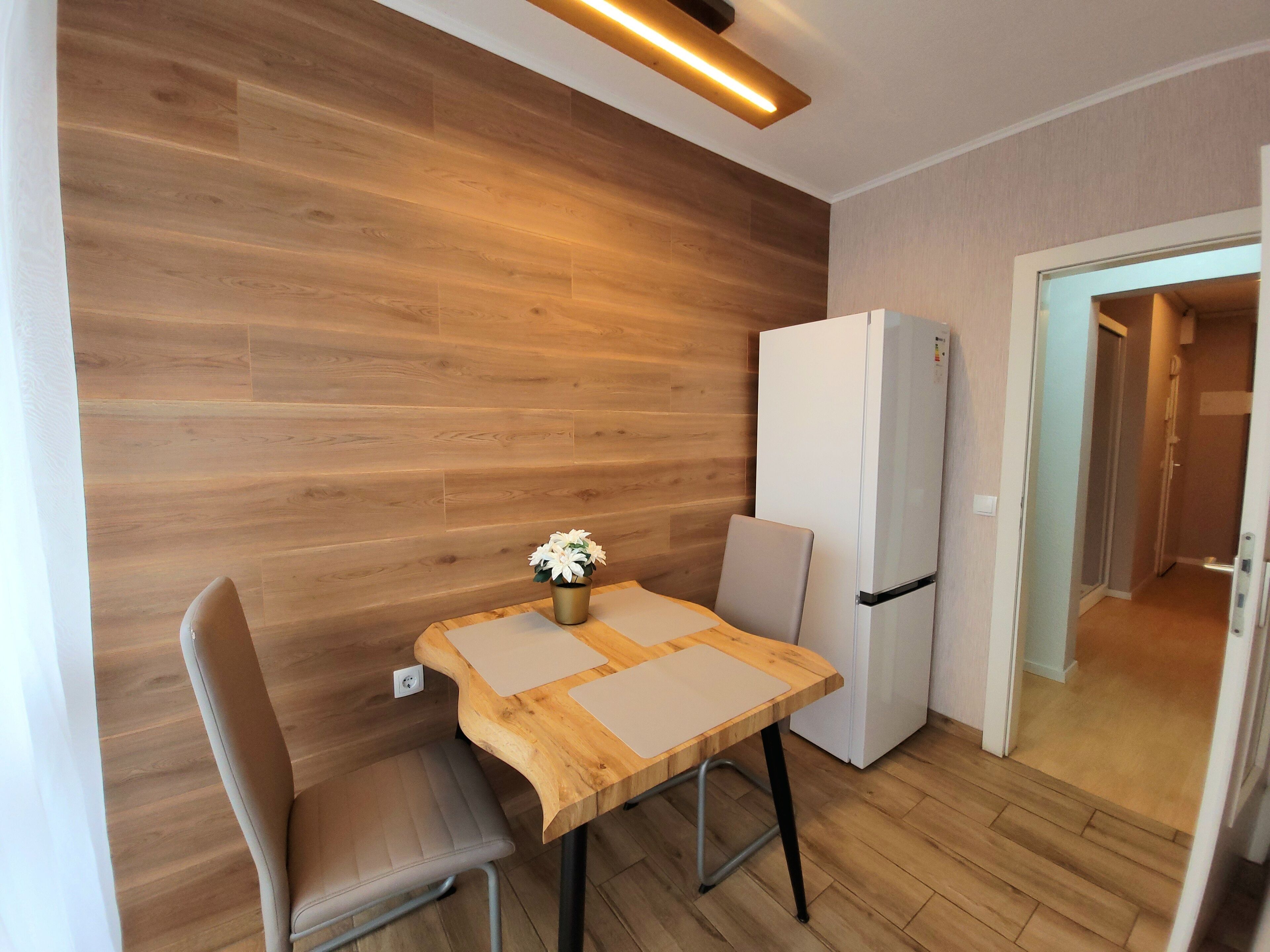 Eine kleine Küchenzeile mit Holztisch, einem Stuhl, einem Kühlschrank und einem Blumentopf.