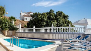A pool with lounge chairs, a white fence, and a building in the background.