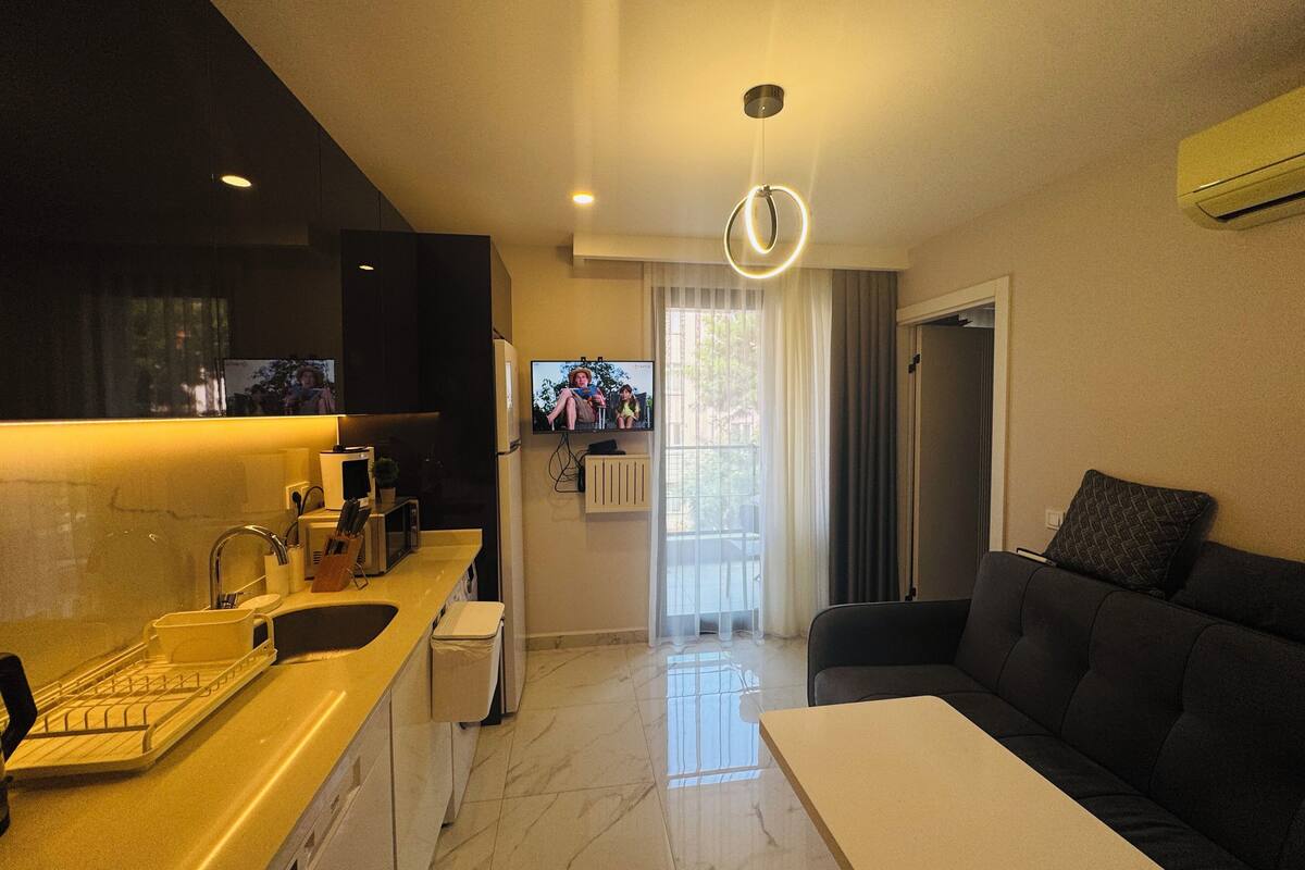 A modern kitchen with a built-in oven, a microwave, and a sink. There is a dining area with a table and a sofa.