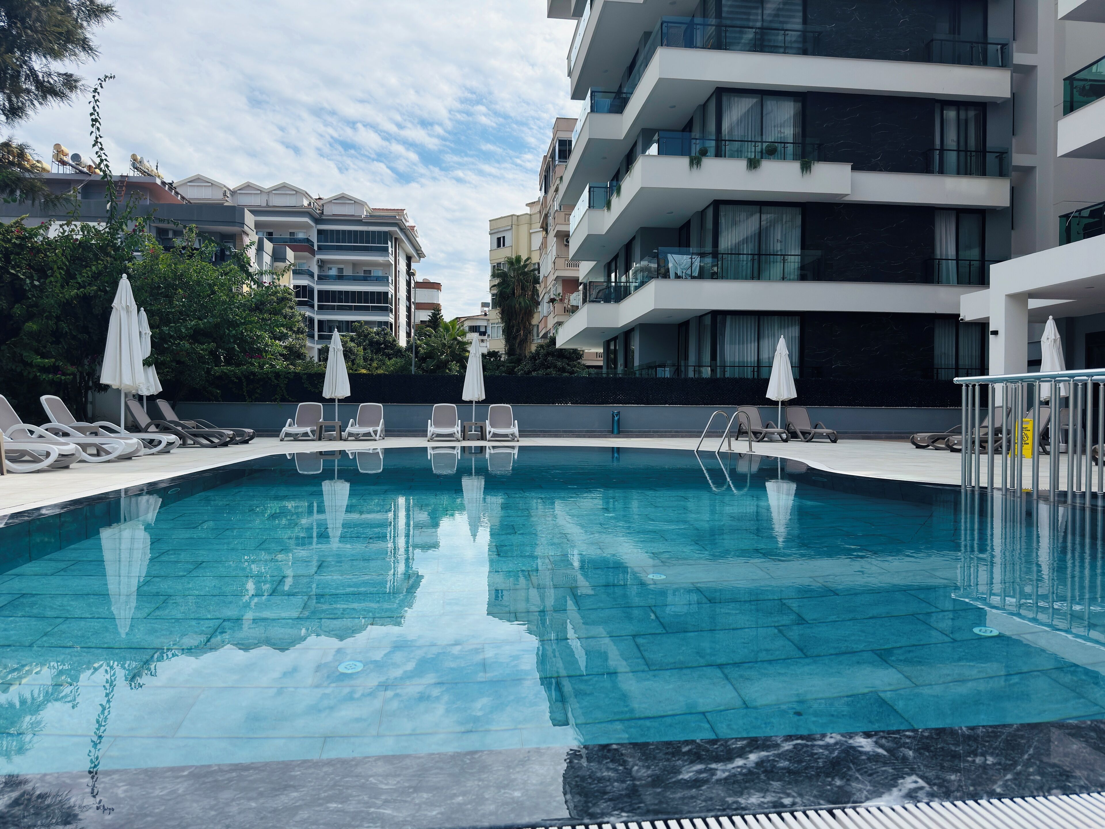 A swimming pool with lounge chairs and umbrellas, surrounded by modern buildings.
