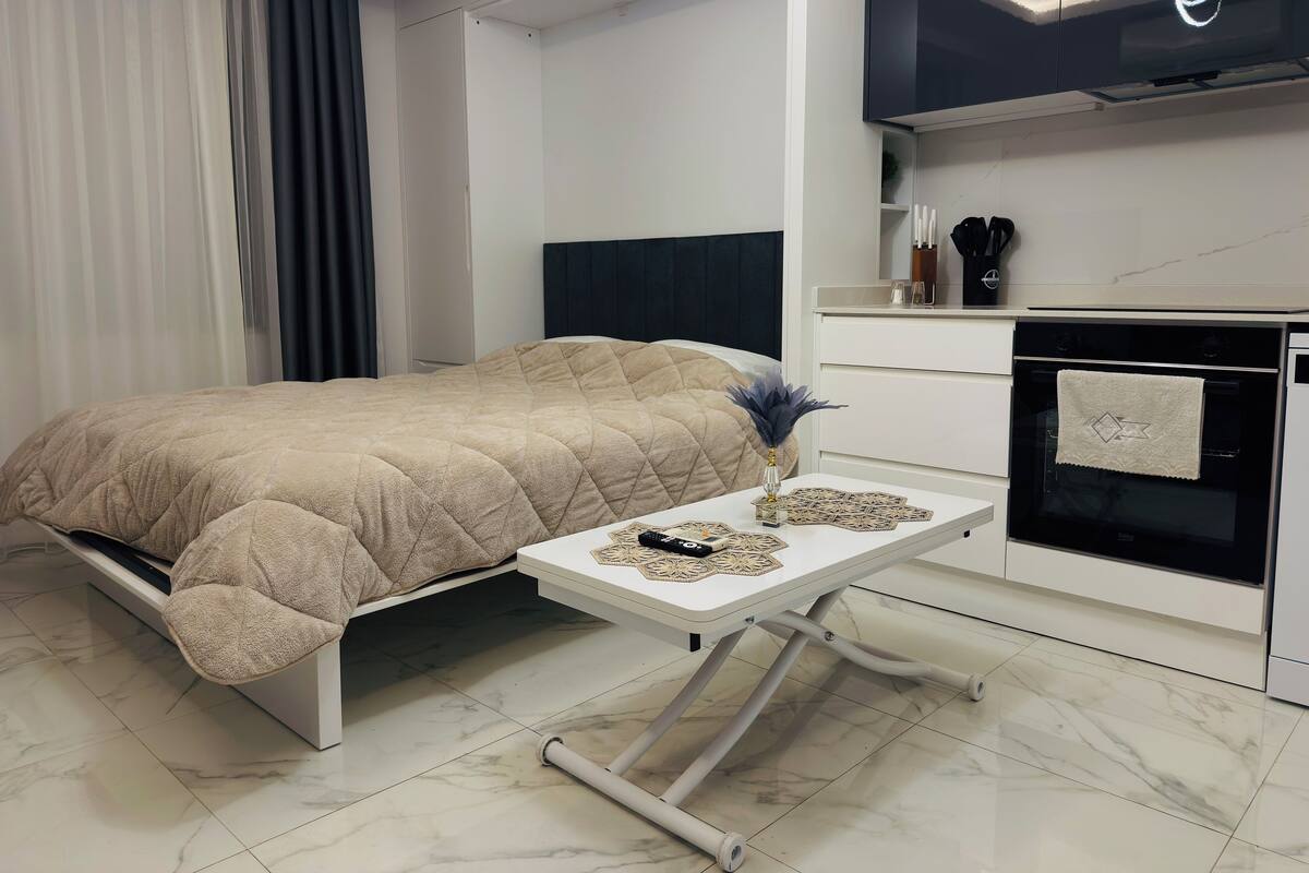 A modern bedroom with a bed, bedside table, and a built-in oven.