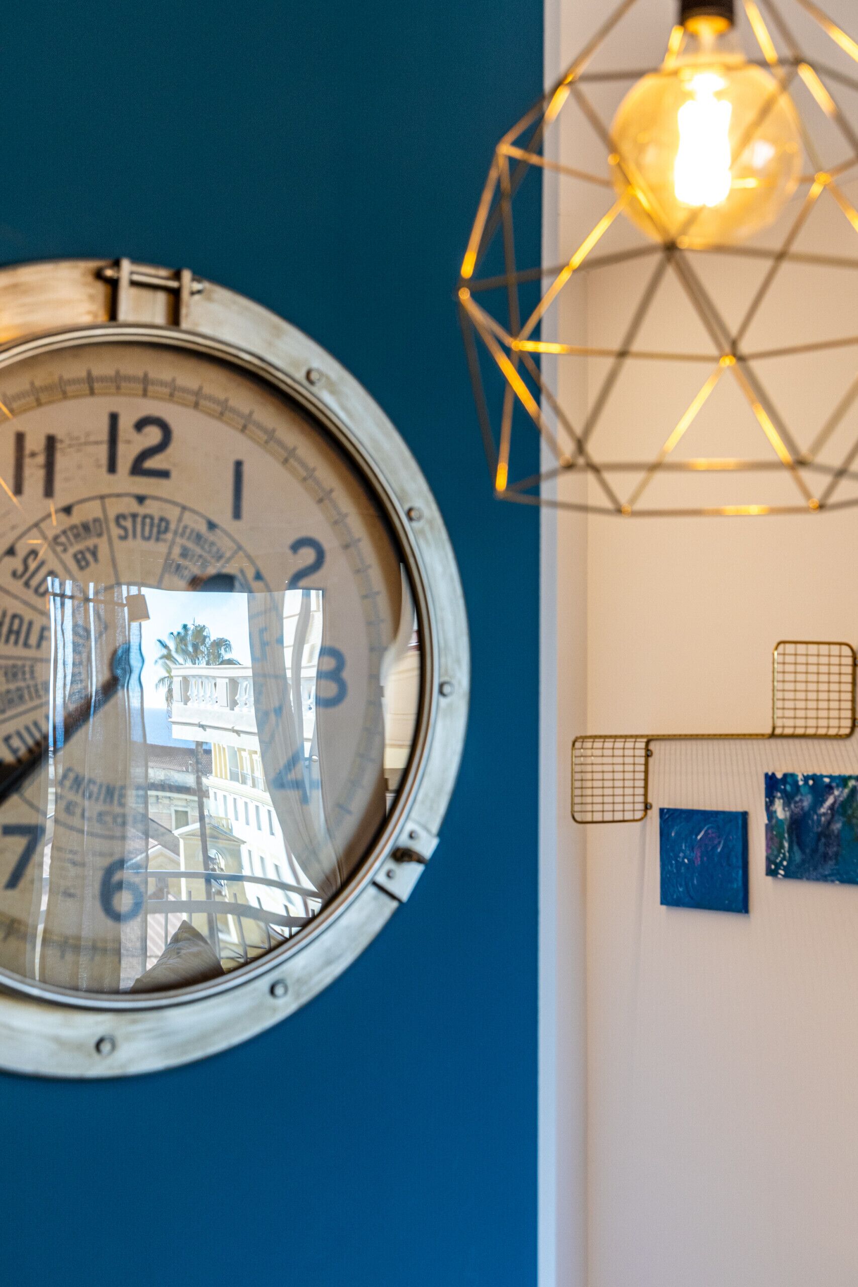 A wall-mounted clock with a nautical theme, a geometric light fixture, and a framed artwork.