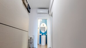 Um corredor estreito com parede branca e uma porta no final que dá para um banheiro.