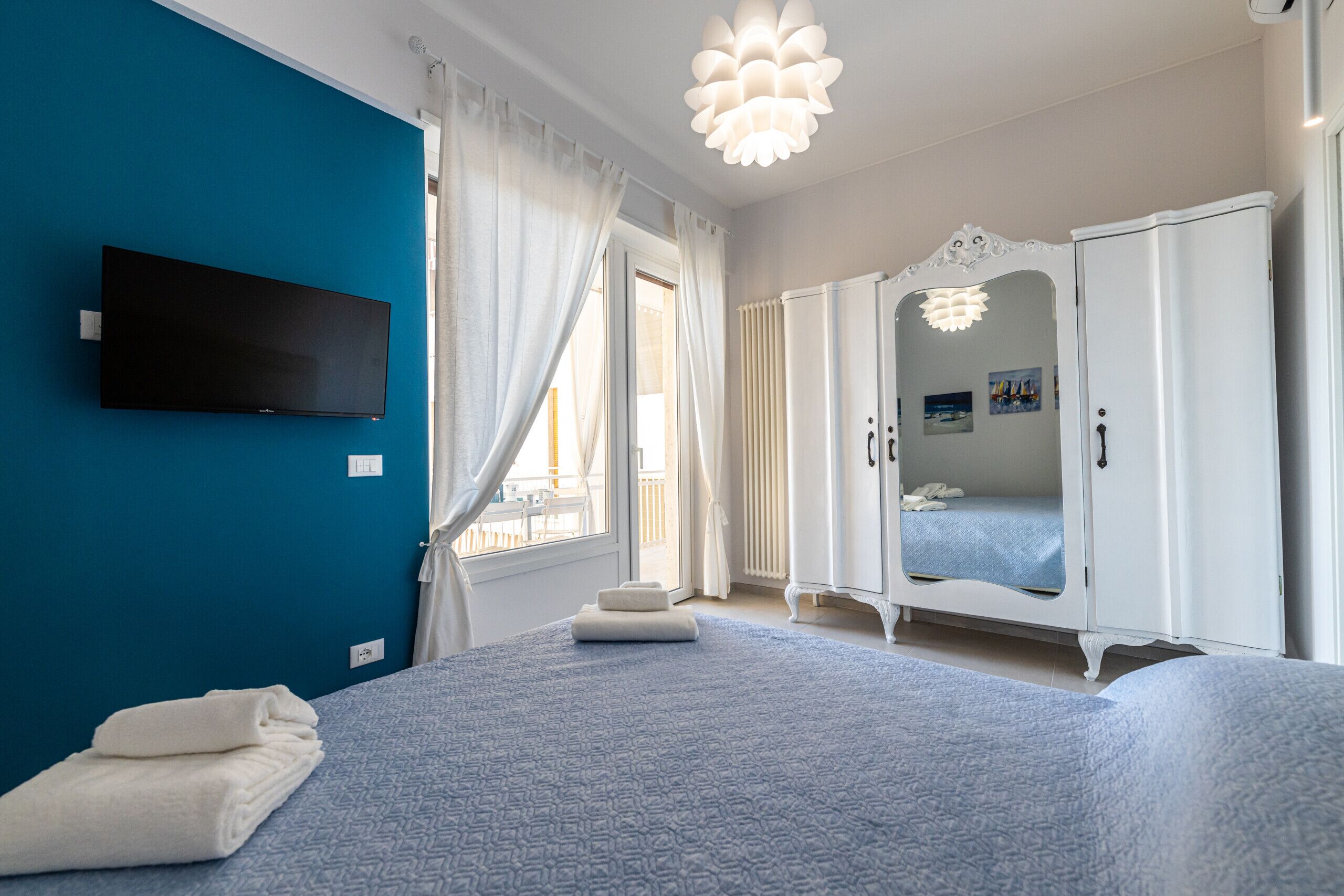 A bedroom with a bed, a wardrobe, a television, and a window with curtains.