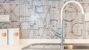 Cozinha com pia de aço inoxidável, torneira branca e backsplash com padrão de planta baixa. Duas embalagens brancas com alças e etiquetas estão sobre o balcão.