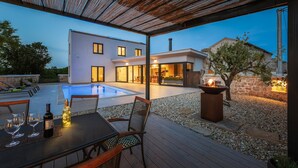A modern outdoor pool area with a wooden deck, seating, and a fire feature. - Villa 115 (100401-K1) - Visnjan (Porec) (Visnjan (Porec))