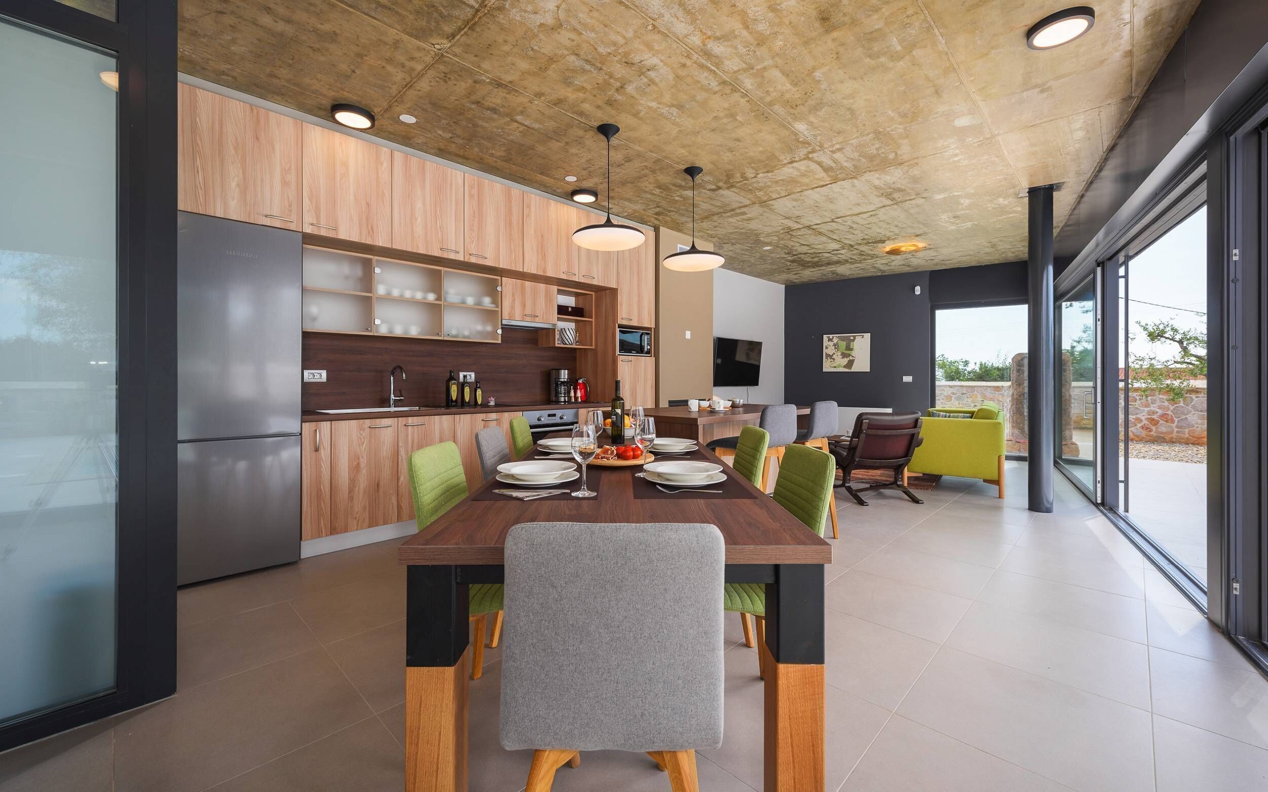 A modern kitchen with wooden cabinets, a dining area with a wooden table and chairs, and a large window offering a view of the outdoors.