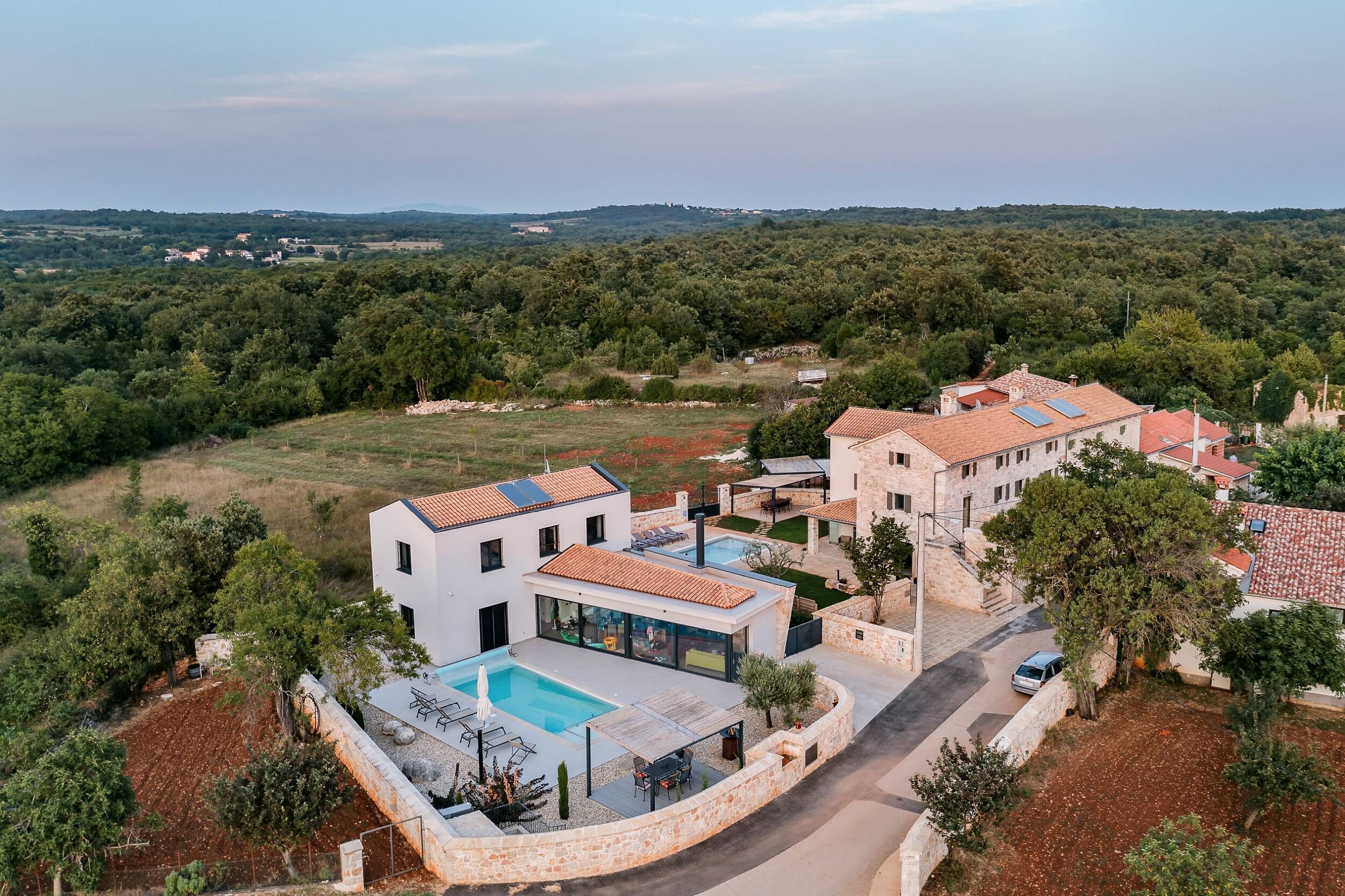 A modern villa with a swimming pool, stone walls, and a view of the surrounding forest.