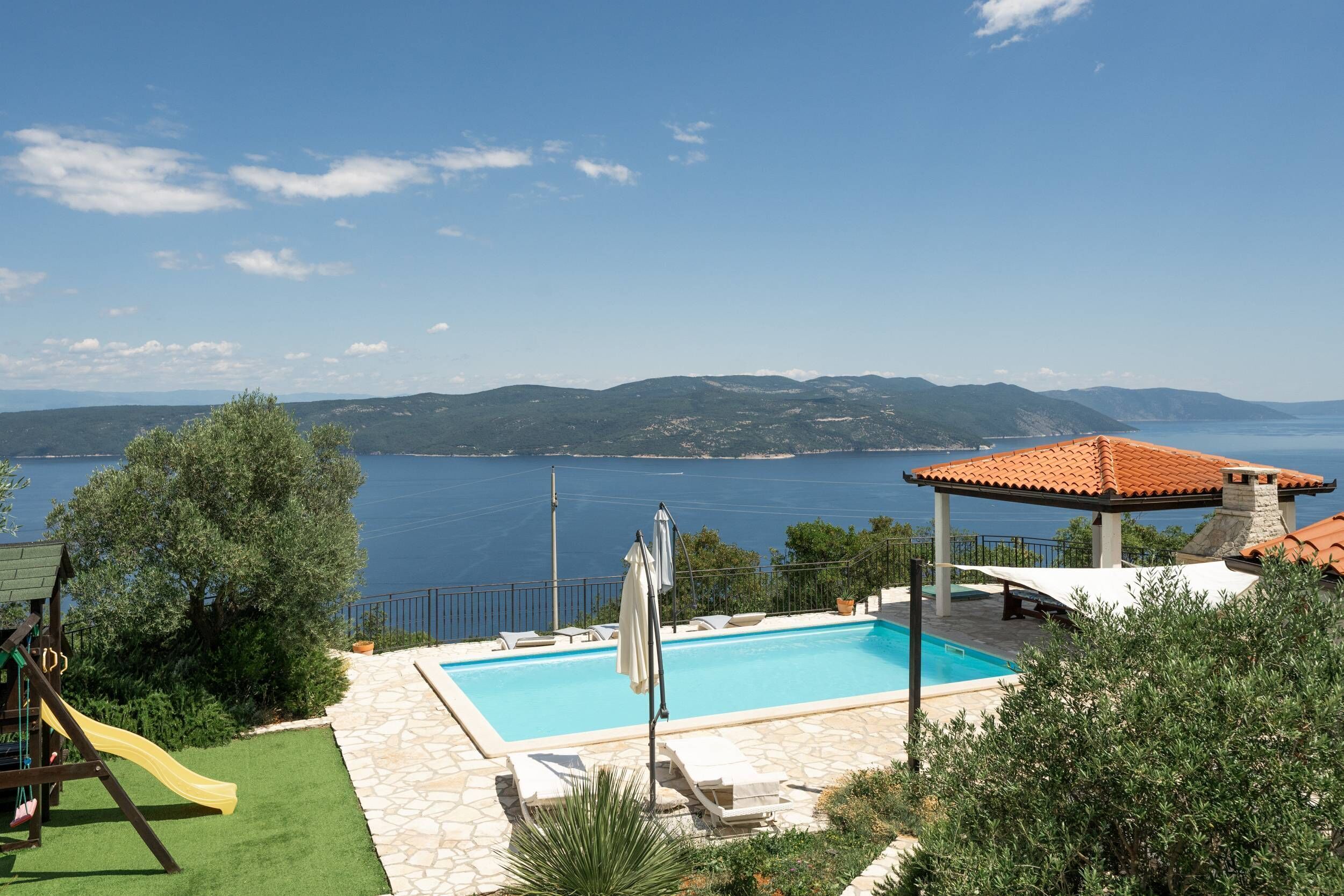 Zona de piscina con vistas al mar, un pabellón y una estructura de juegos infantiles.