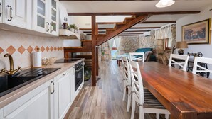 Une cuisine avec des meubles blancs, une table à manger en bois et un mur en pierre en arrière-plan.