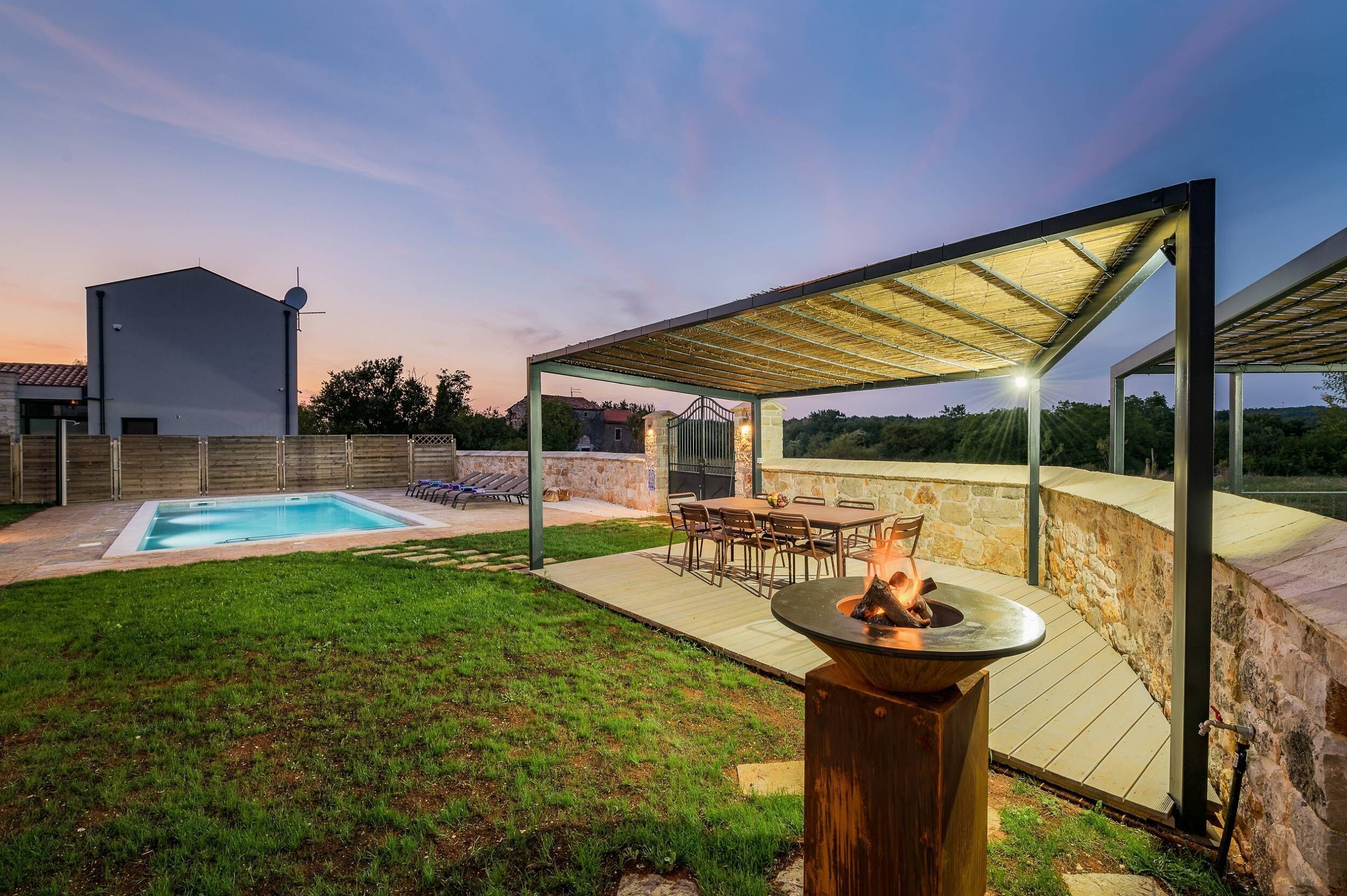 A backyard with a swimming pool, a covered patio, and a fire pit.