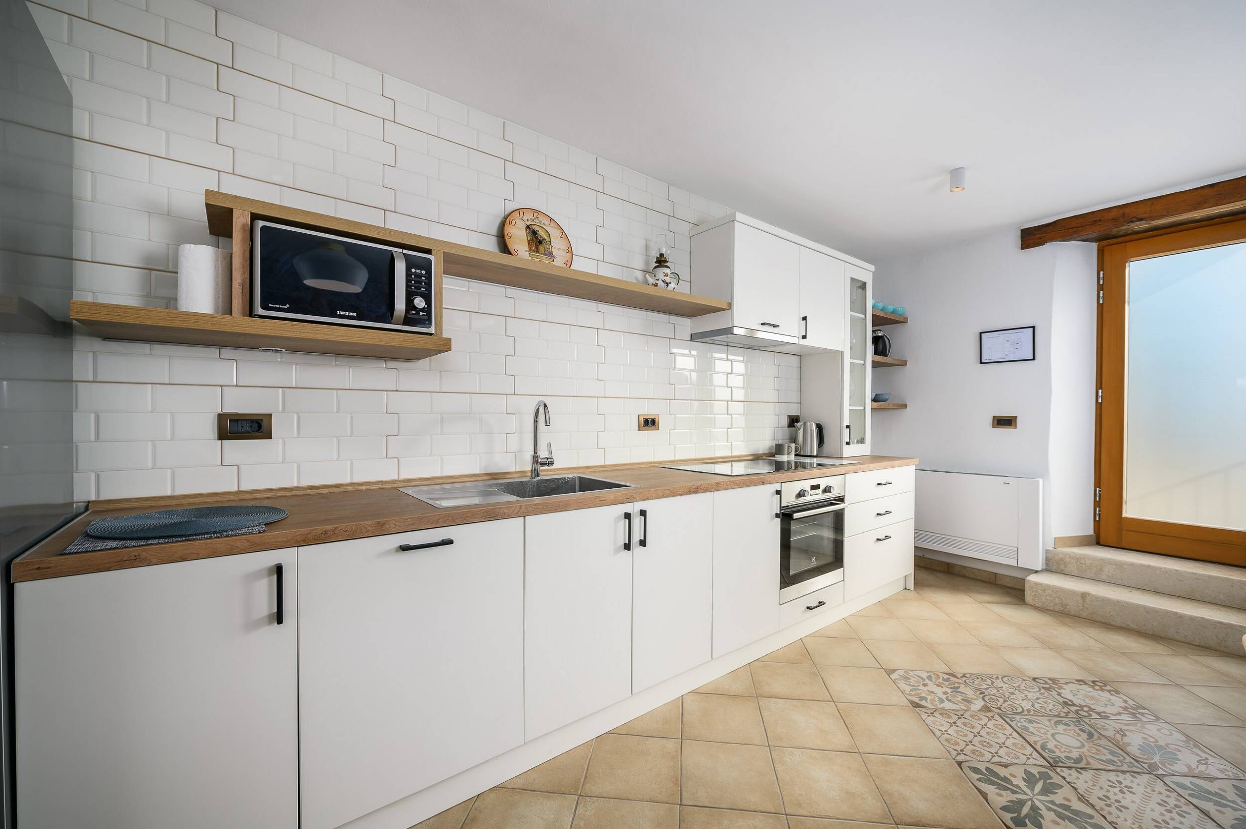 A modern kitchen with white cabinets, a wooden countertop, a microwave, and a sink.