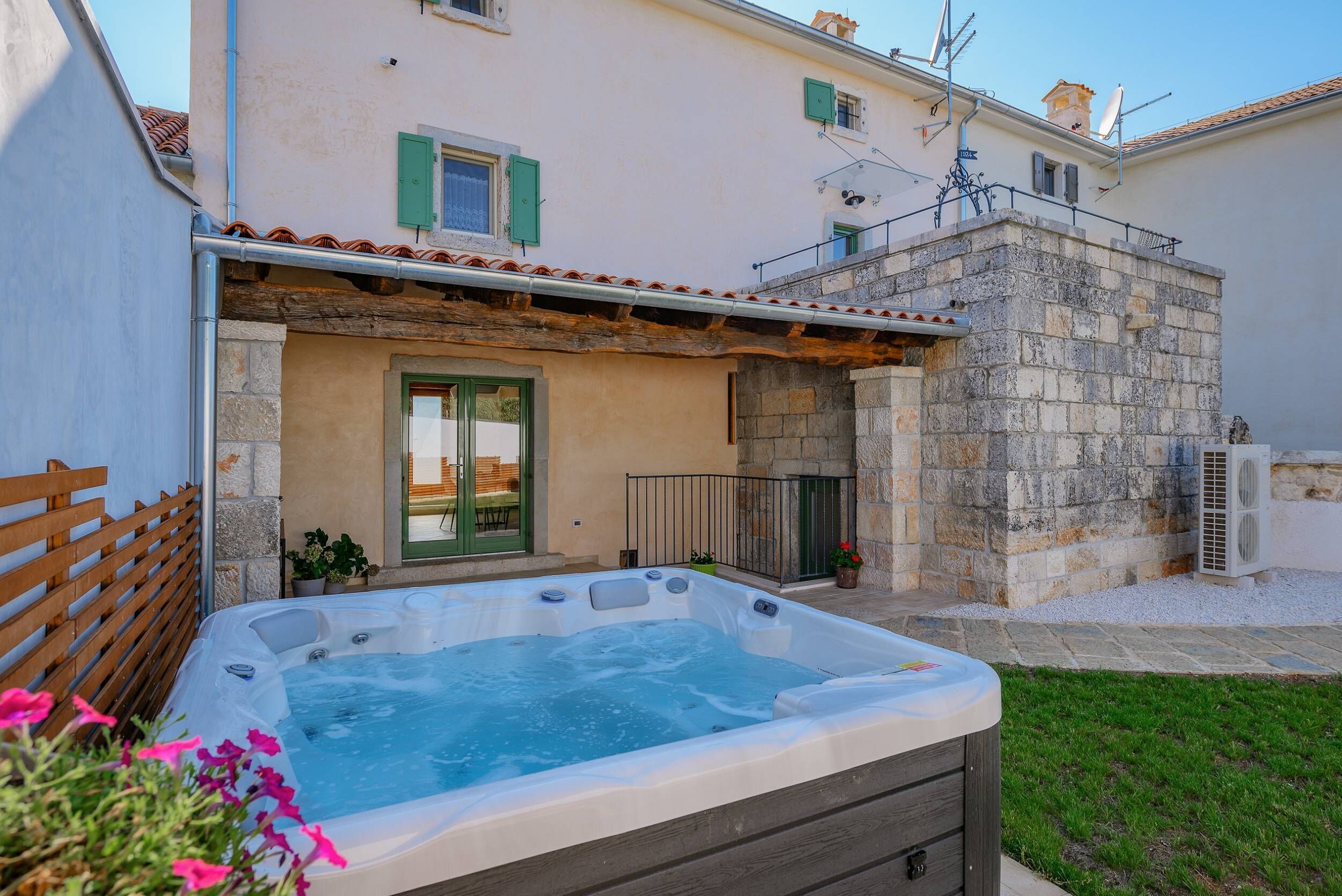 A residential building with a stone exterior, a wooden deck, and a hot tub in the foreground.